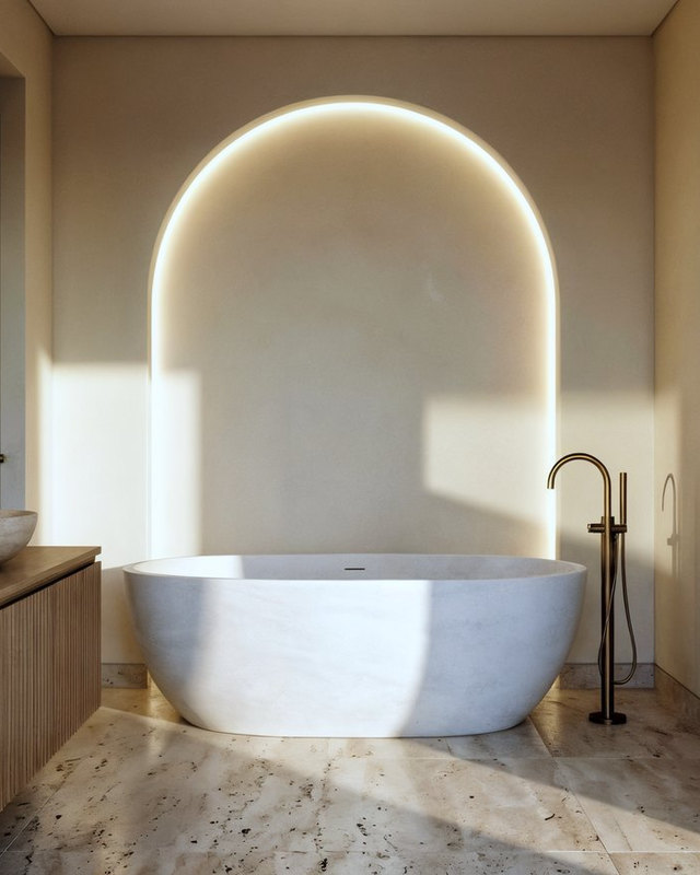 A bathroom with a backlit arched niche behind a freestanding stone tub, brass fixtures and a wall-hung double vanity, Studio Sakaia, Dubai