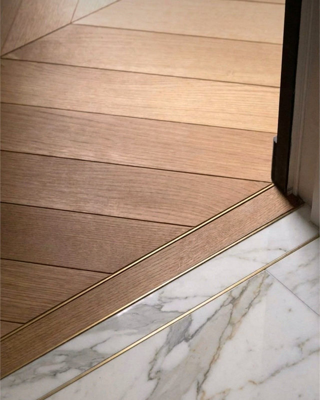 Engineered oak flooring meeting marble at a brass-lined threshold, warm herringbone detail, Studio Sakaia, Dubai