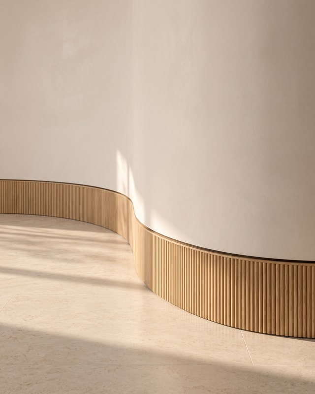 A reeded white oak baseboard following a curved plaster wall above a honed limestone floor in warm afternoon sun, design visualisation by Studio Sakaia.