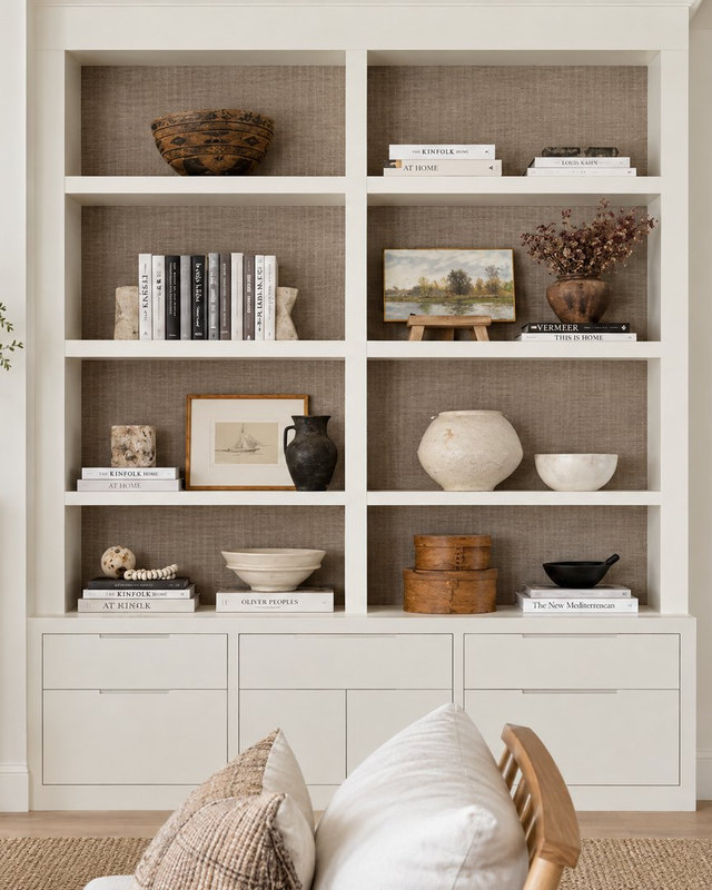 Sakaia visualisation: an ivory painted built-in bookcase with square shelf openings, styled with staggered books, ceramics, a leaning framed sketch and landscape painting, and cabinet drawers below.