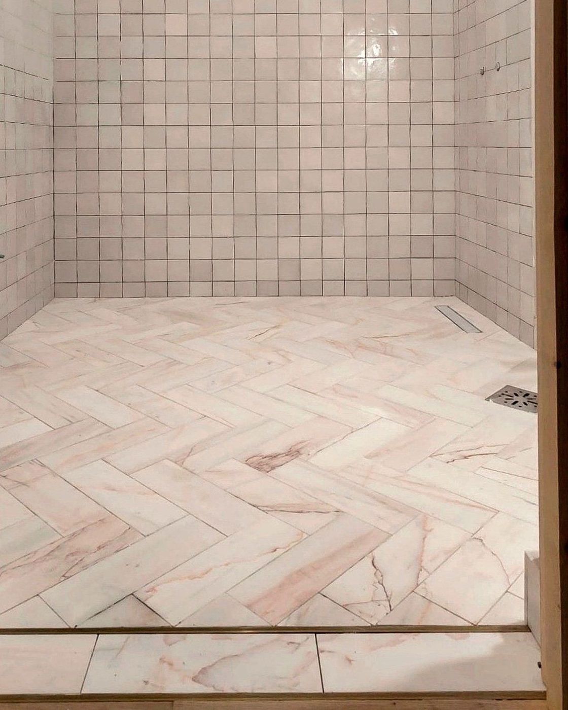A marble-tiled shower with a herringbone floor meeting a brass threshold at the doorway, Studio Sakaia, Dubai