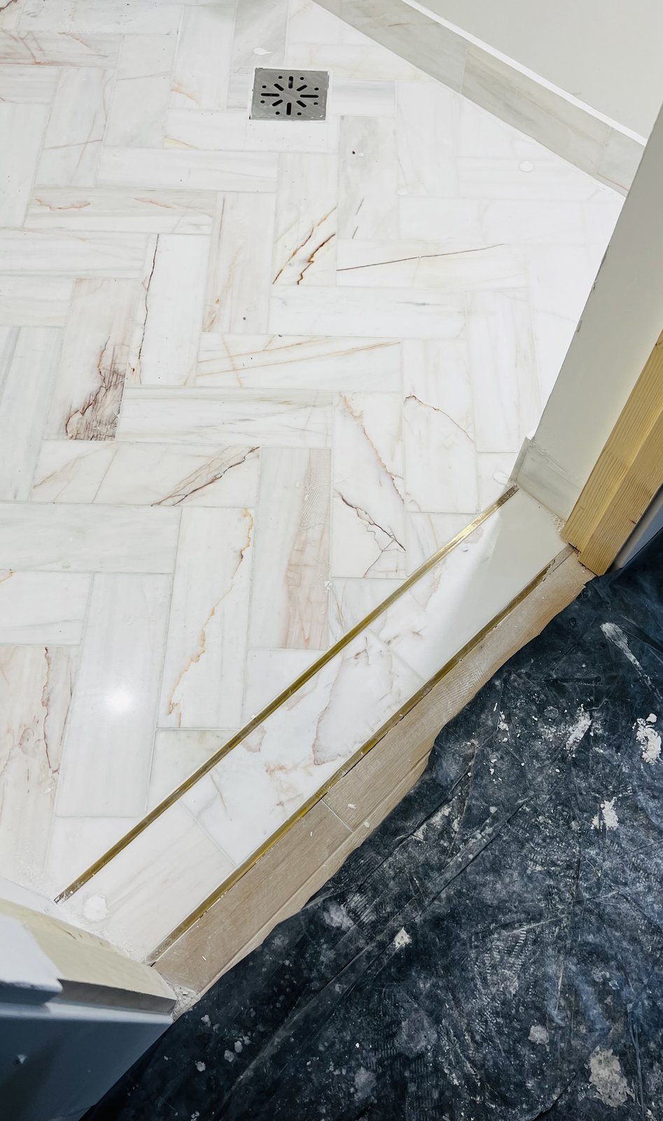 A macro detail of a brass bar threshold between a herringbone oak floor and marble bathroom tile, from Studio Sakaia's own Dubai renovation