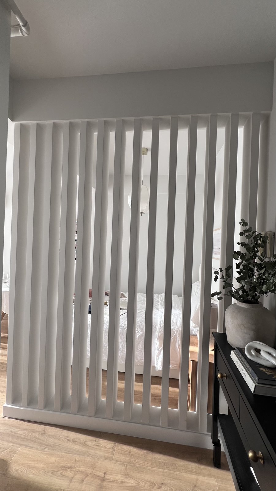 A finished slatted timber room divider in a styled Dubai bedroom, warm lamplight through the slats, Studio Sakaia, Dubai