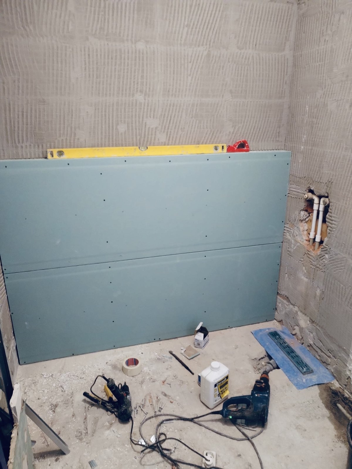 A moisture-resistant board set and levelled against the prepared shower wall, with the linear drain waiting on the floor, Studio Sakaia