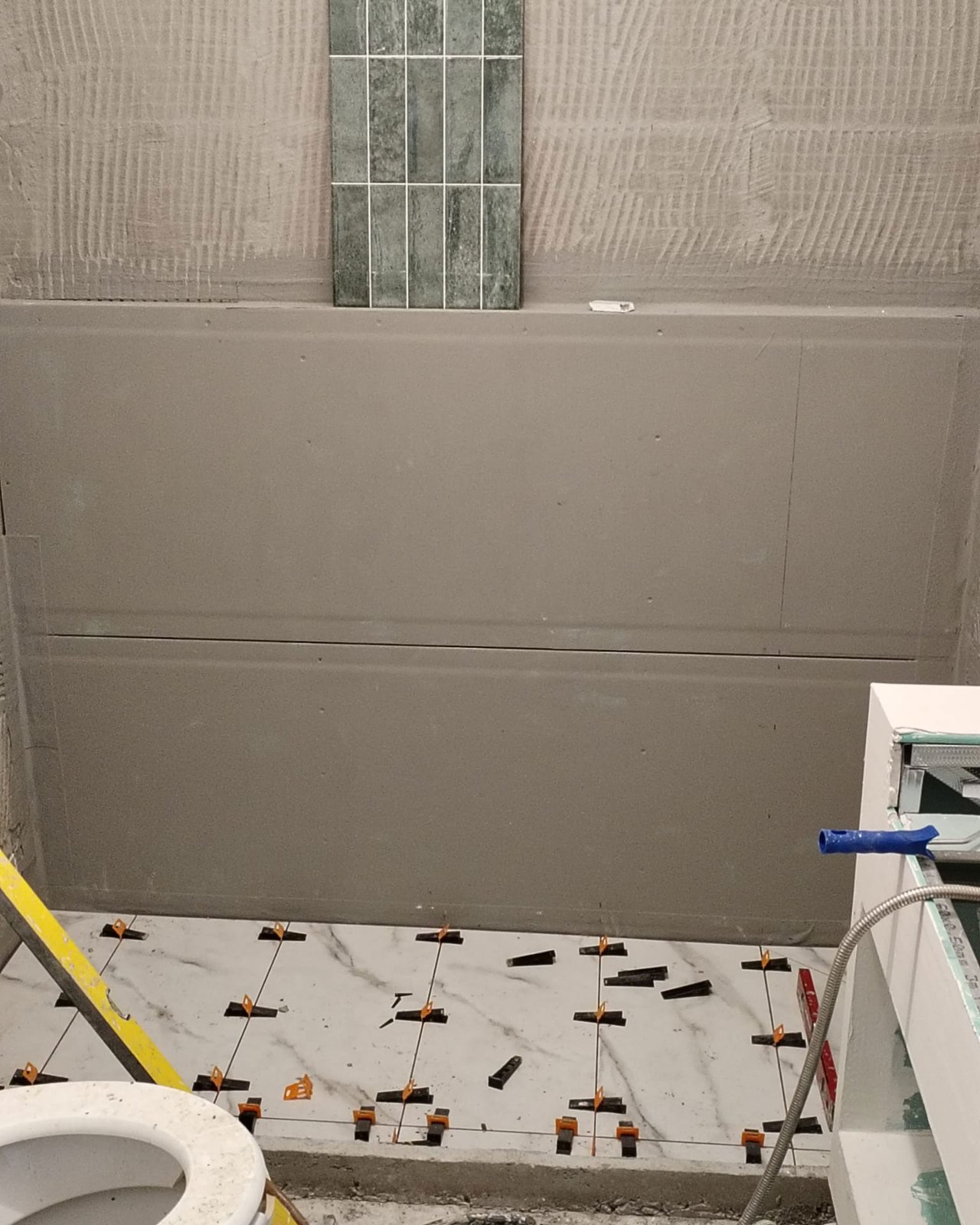 The tanked wall with a single run of tile held up to check the setting-out, and the marble floor going down on levelling clips, Studio Sakaia