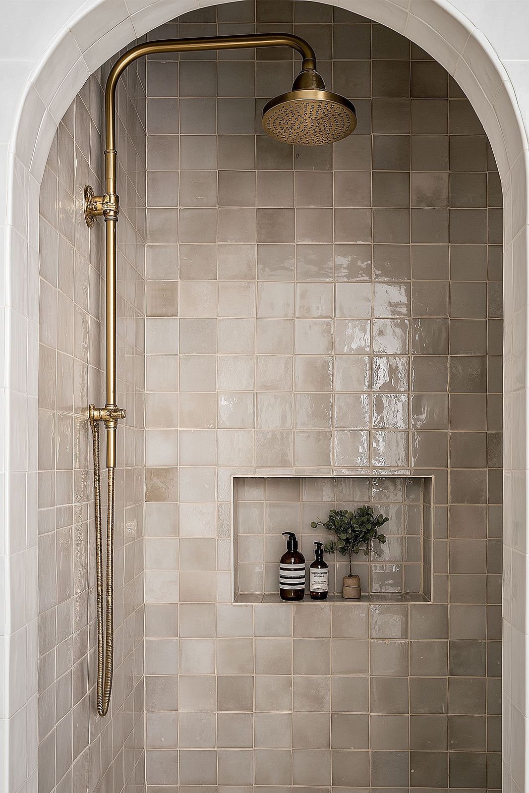An arched shower niche in a tiled wall with a brass rainfall shower, warm light, from Studio Sakaia's own Dubai renovation