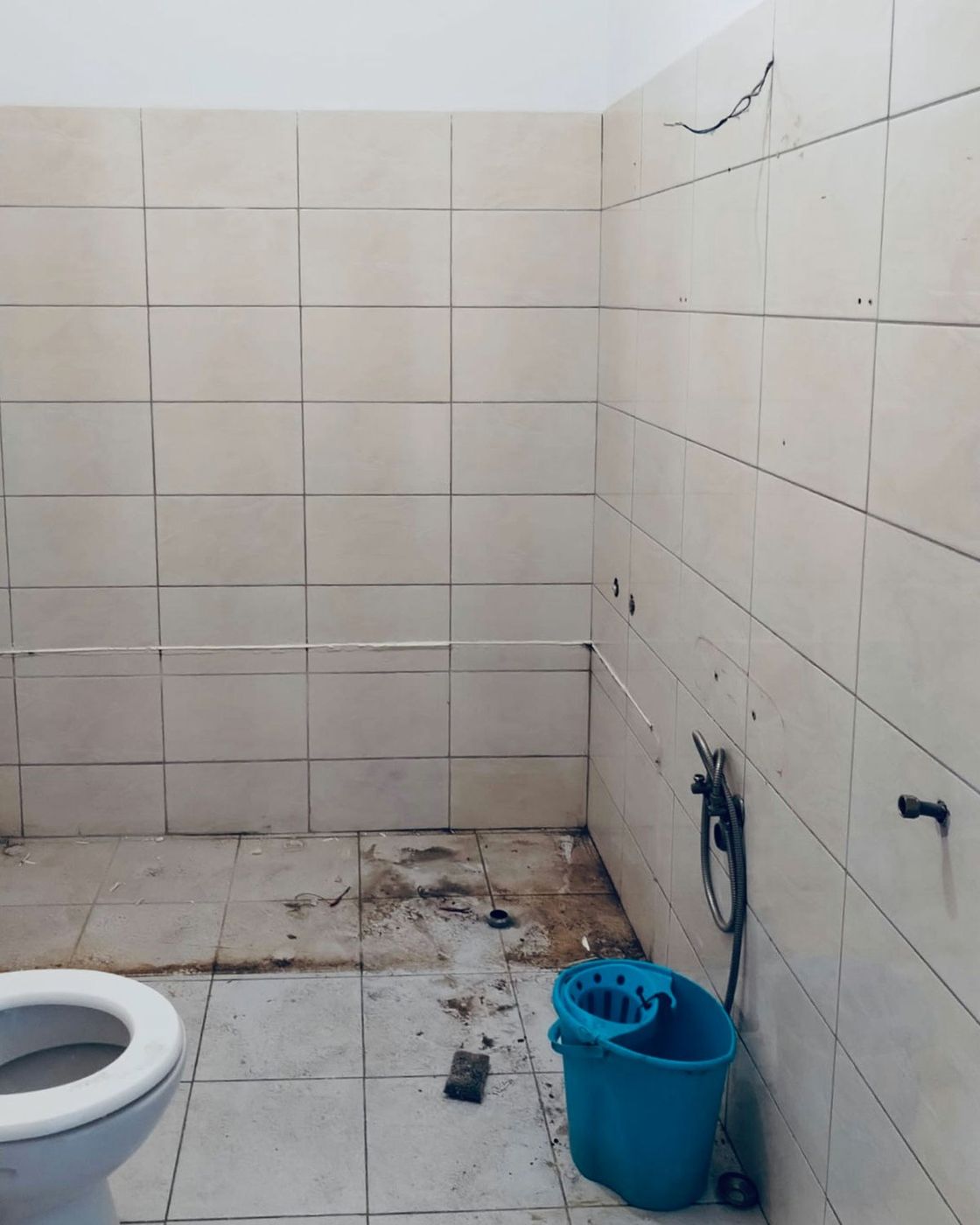 The bathroom before, dated cream tile, a bare toilet and a cleaning bucket, Studio Sakaia, Dubai