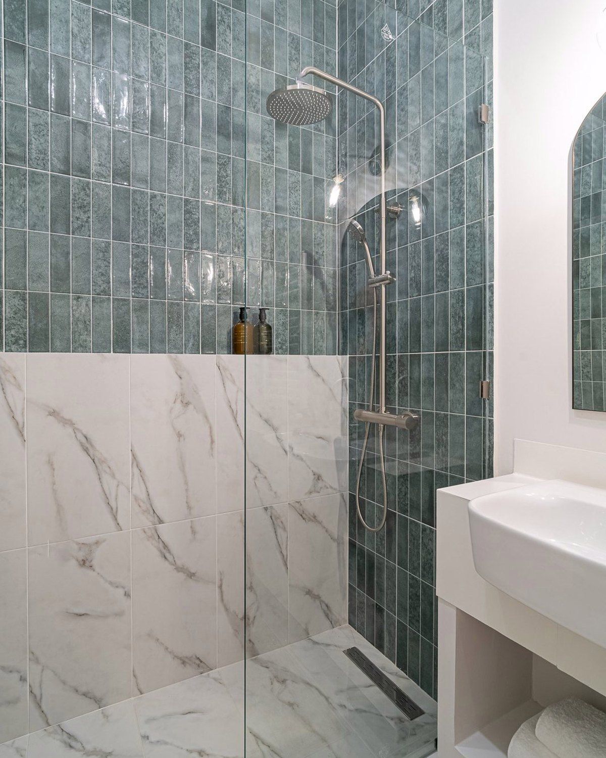 A finished bathroom shower in fluted teal tile and white marble, a rain shower head and brushed nickel column, Studio Sakaia, Dubai
