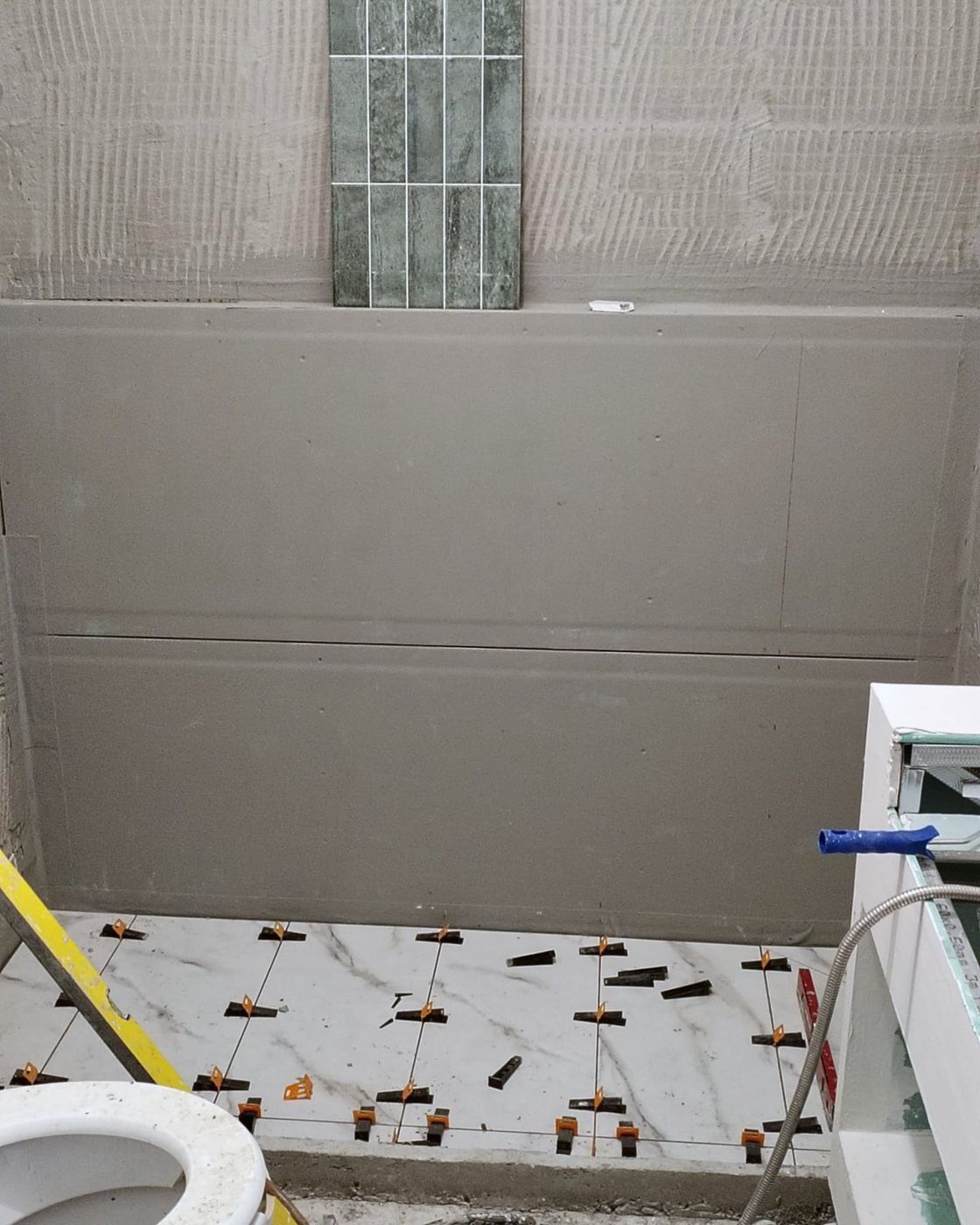 Marble floor tiles going down with levelling clips and a tile sample held against the rendered wall, Studio Sakaia, Dubai