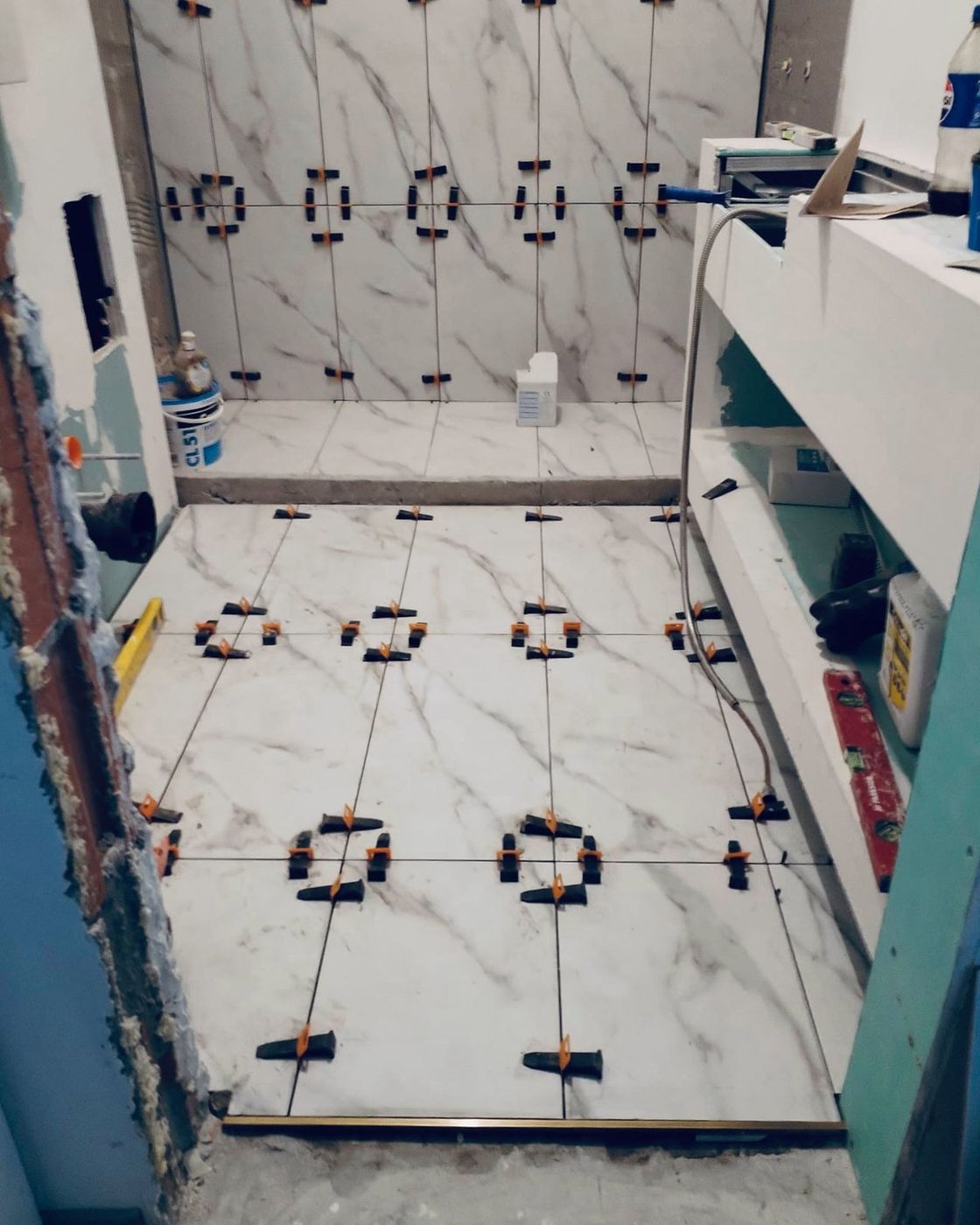 Marble tile going down over levelling clips with the first courses of teal tile started on the wall above, Studio Sakaia, Dubai