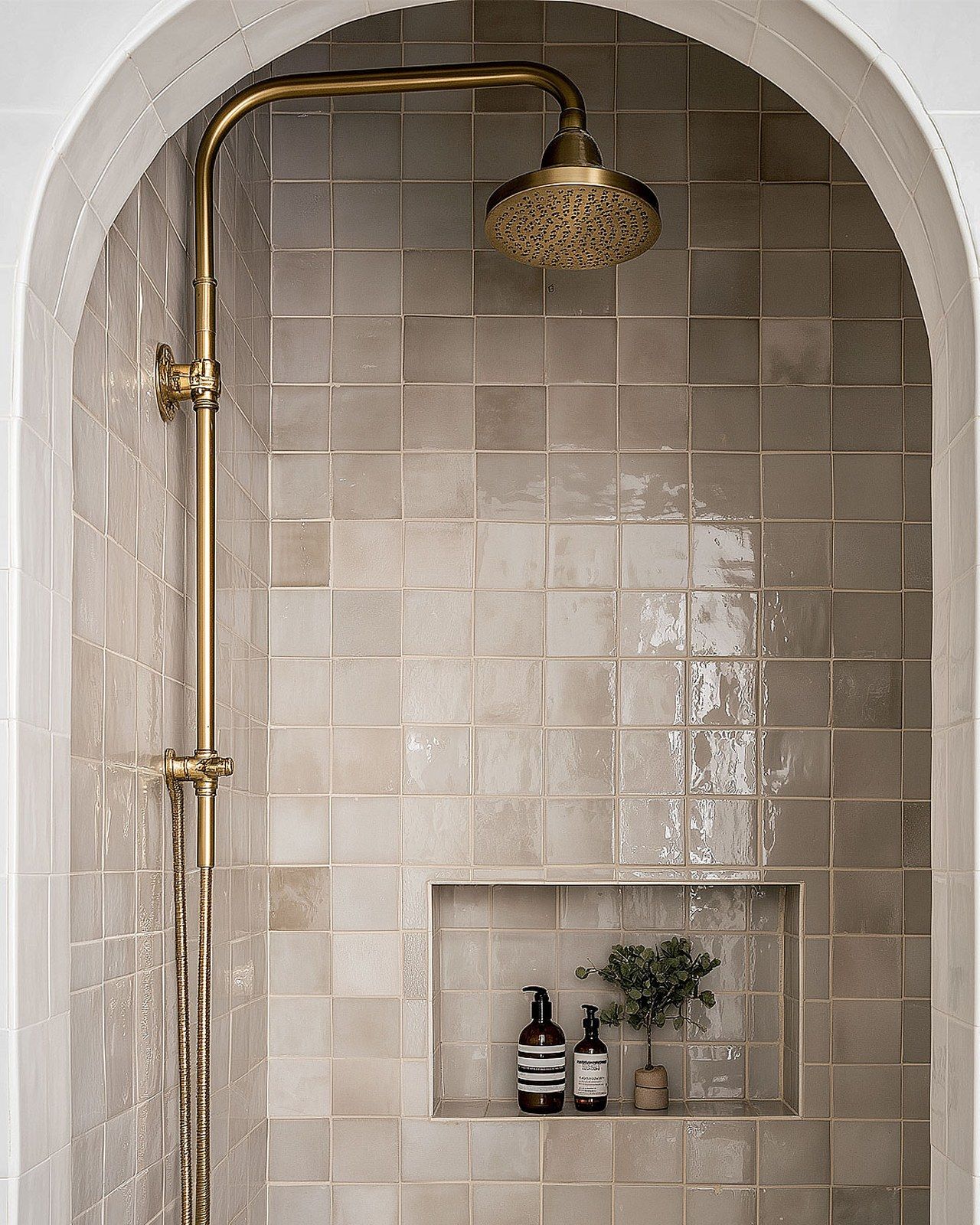 A shower area tiled in Marazzi Gesso zellige-look tile catching the light unevenly, brass rainfall fixture, from Studio Sakaia's own Dubai renovation
