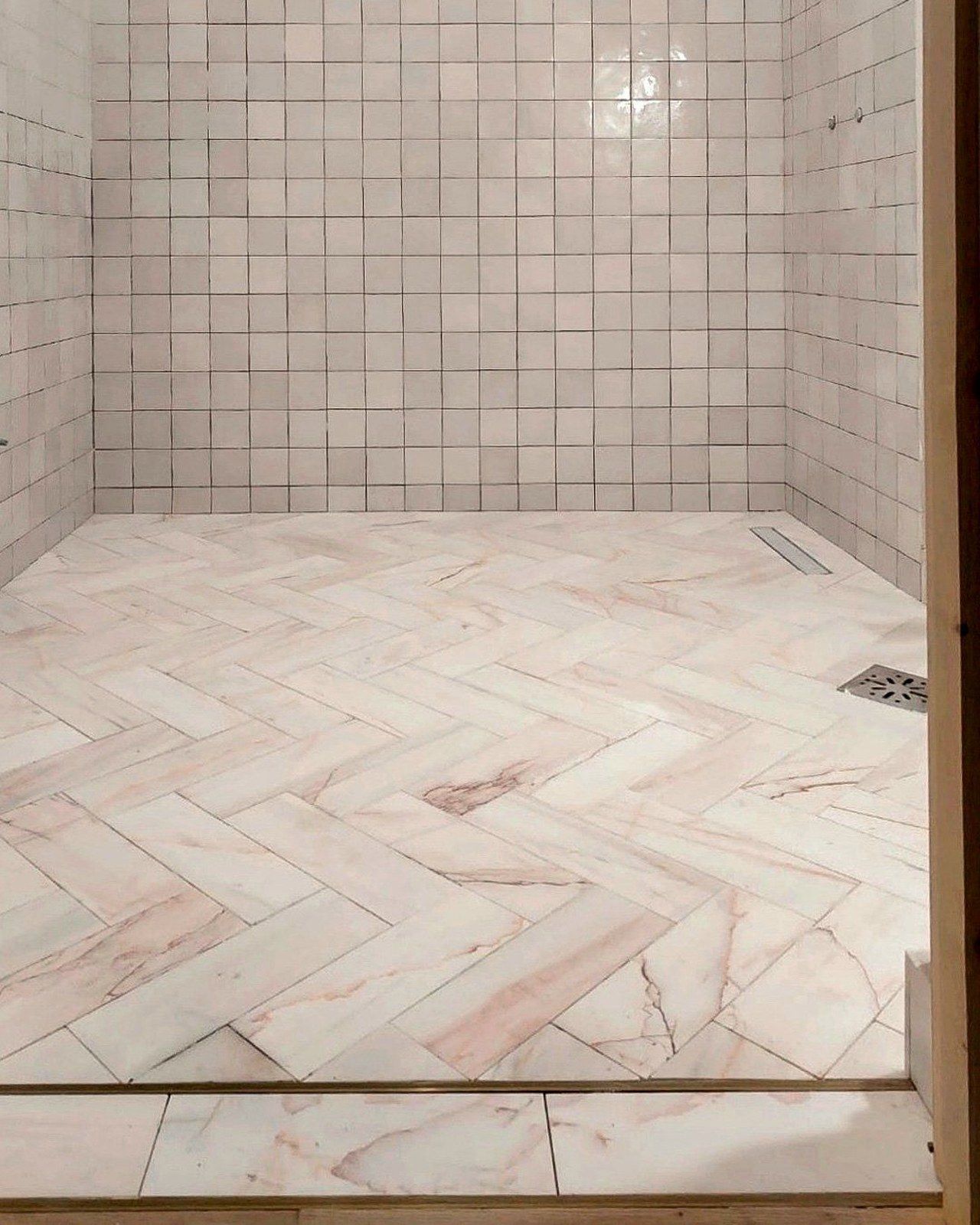 A finished shower floor in herringbone marble meeting a brass threshold strip, Studio Sakaia, Dubai