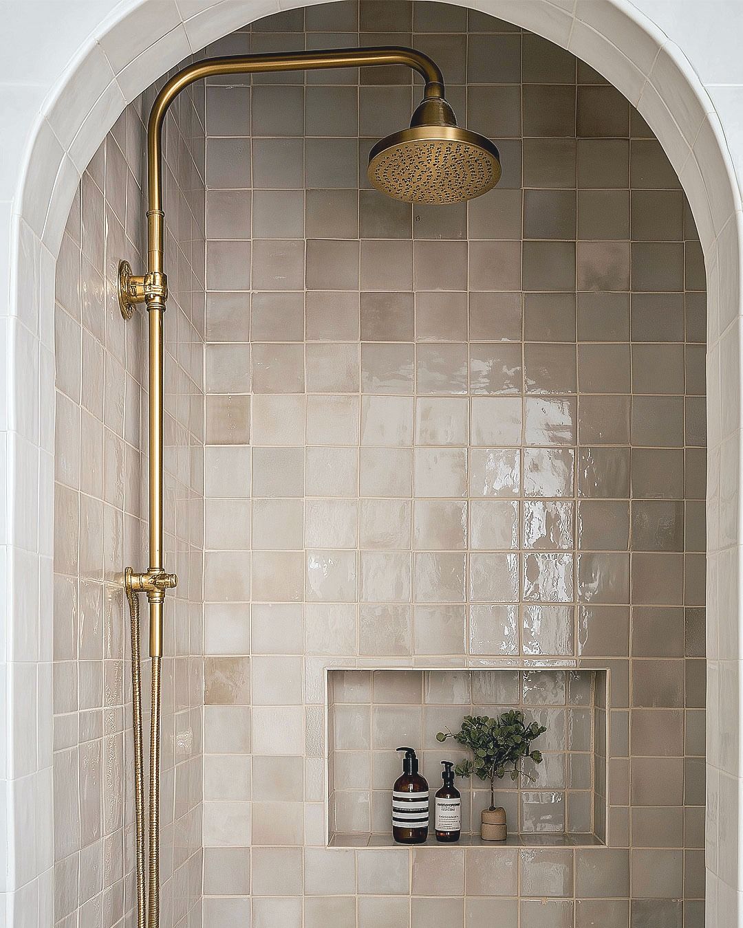 Arched shower design study: glazed square tile, aged brass shower set, tiled storage niche.