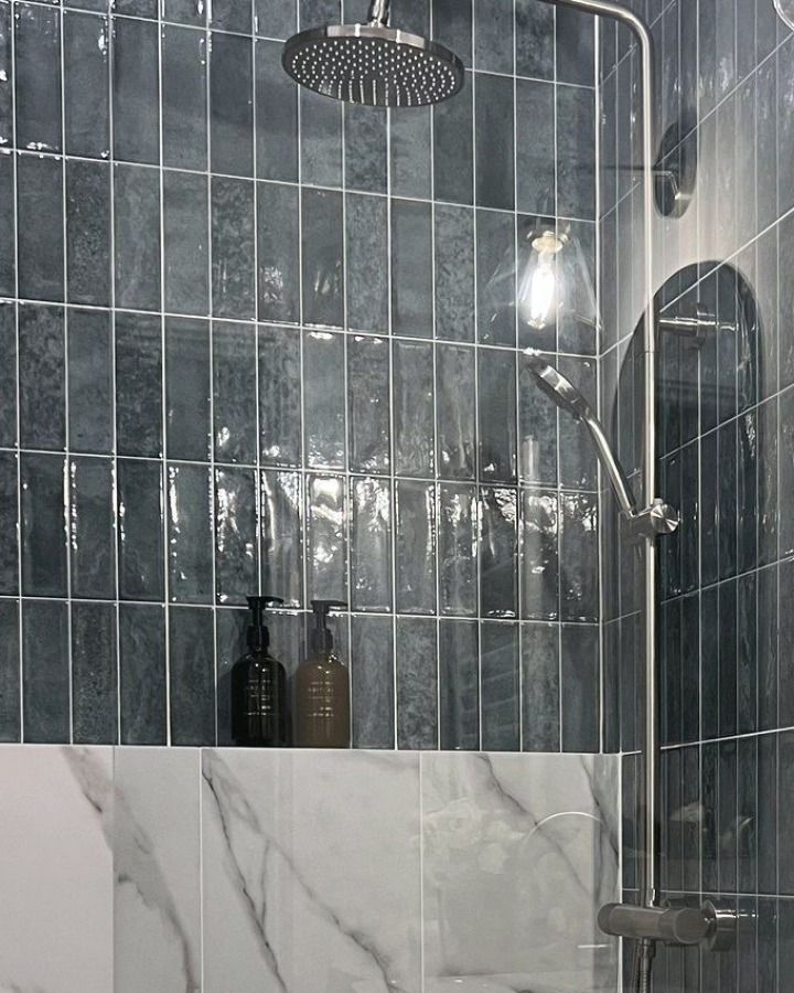 Finished bathroom detail: nickel shower column and rain head against glazed teal vertical tile.