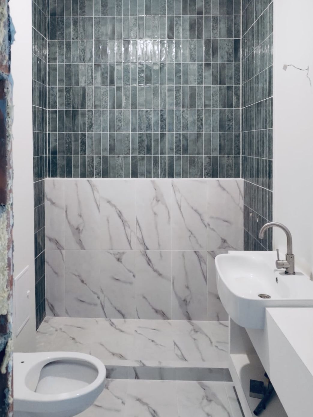 Bathroom mid renovation with glazed teal tile and marble installed, vanity still in build.