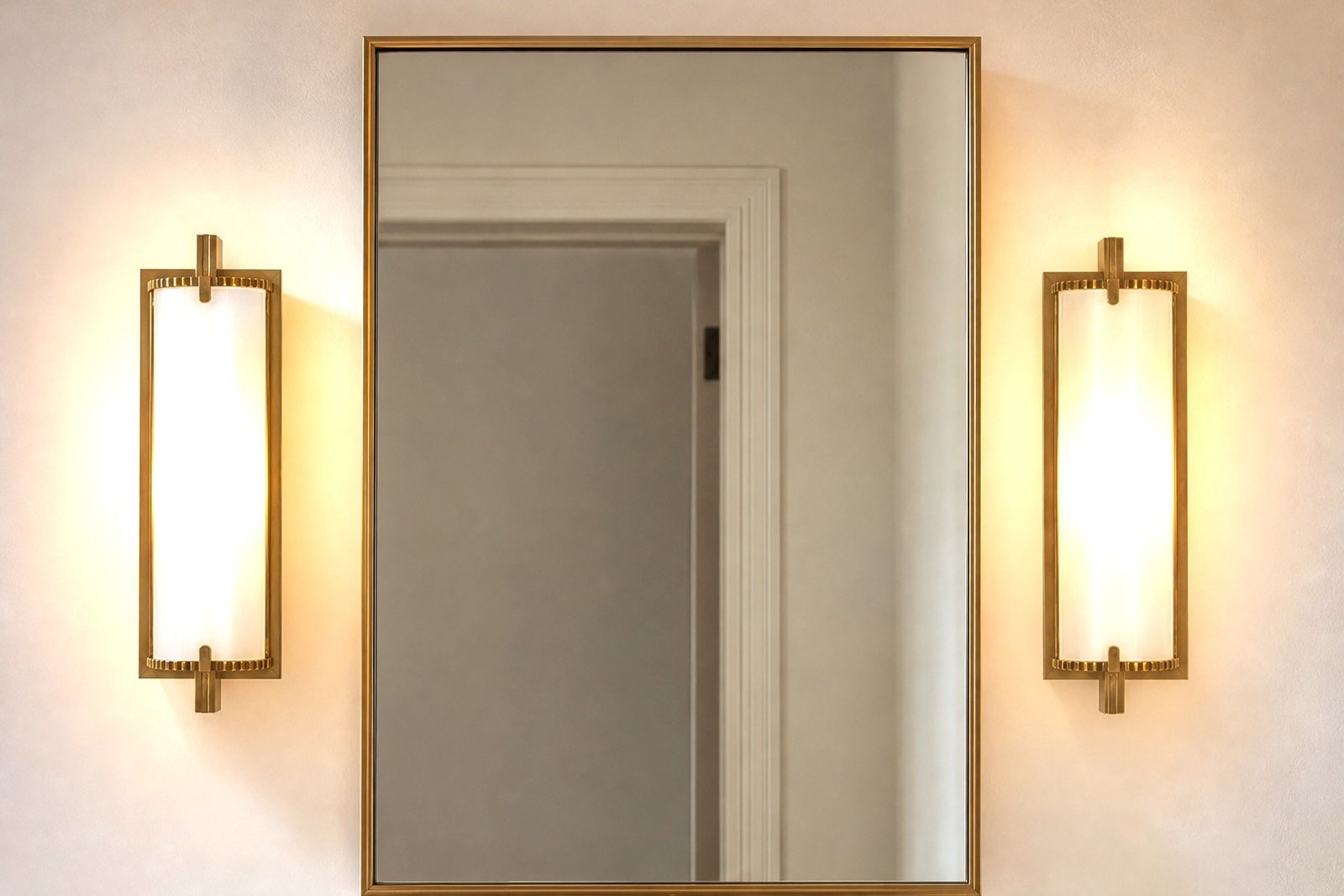 Sakaia visualization: two brass wall sconces lit at face height flanking a bathroom mirror above a marble vanity.