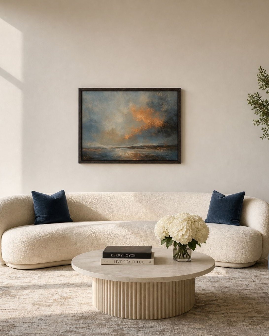 A living room with a curved cream boucle sofa, a dark framed amber and blue seascape above it, a fluted travertine coffee table with white hydrangeas, an olive tree and a Burj Khalifa view through a black steel window, Dubai.