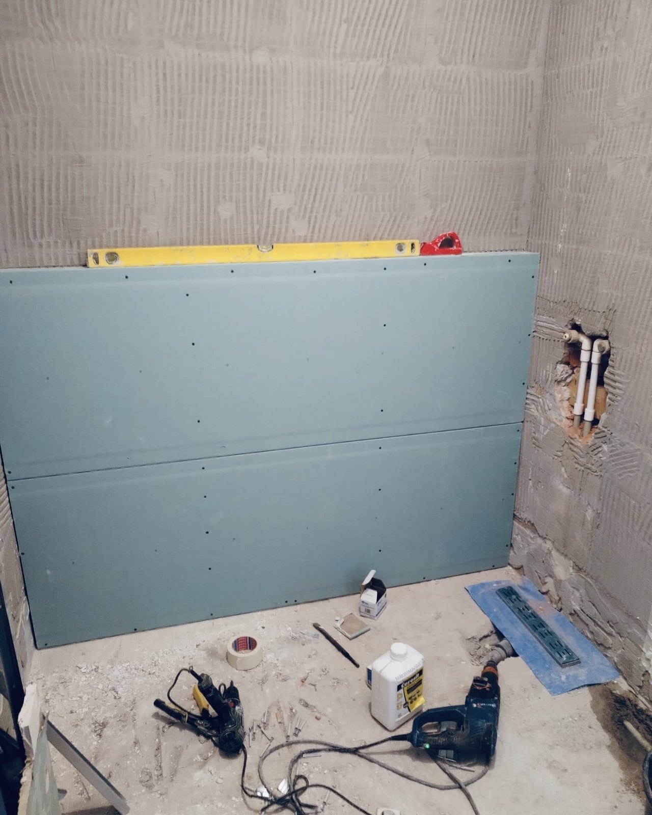 Bathroom under renovation in a Dubai apartment: moisture resistant board fixed to the wall, a spirit level resting on the top edge, pipework left open beside it.