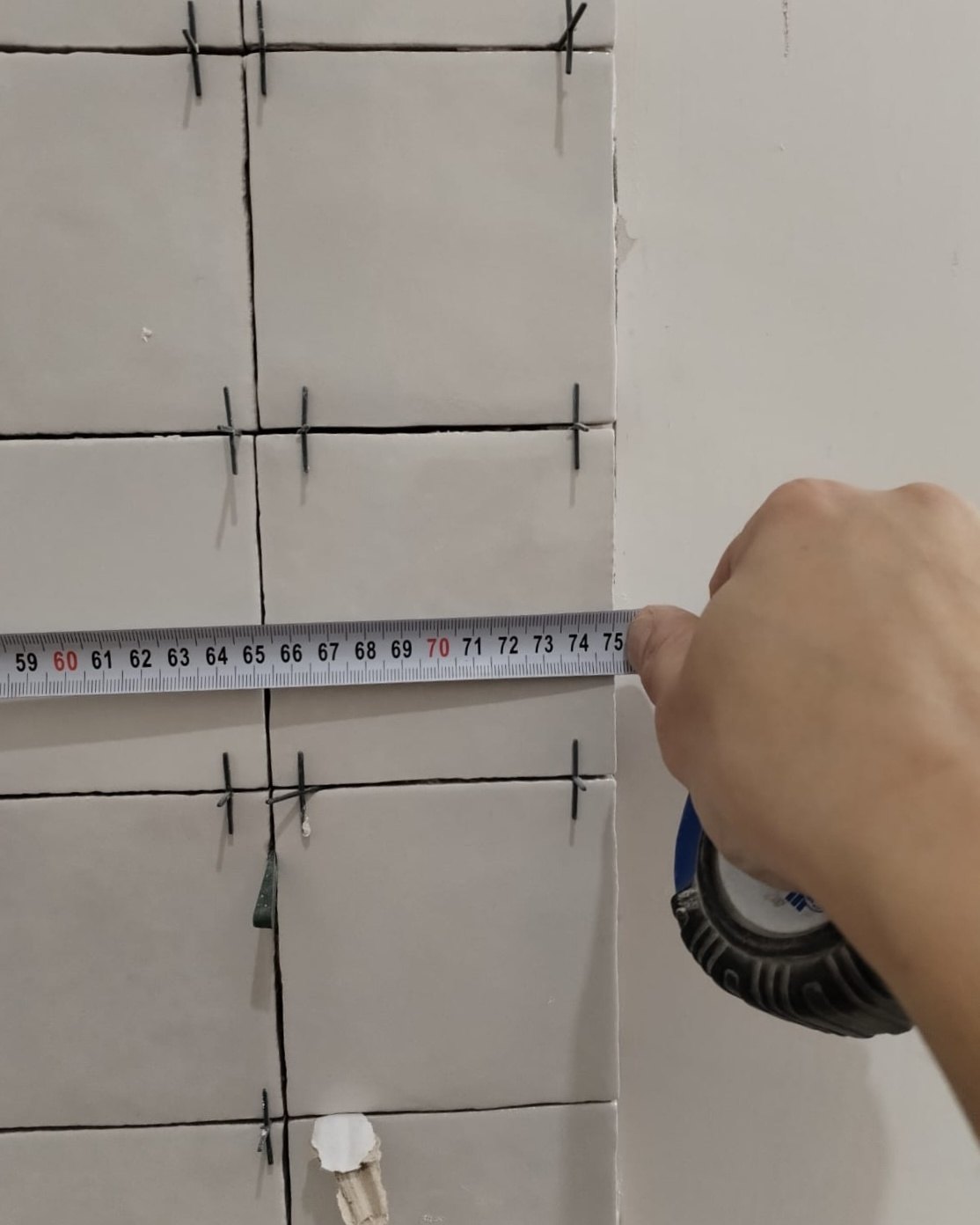 Bathroom under renovation in a Dubai apartment: tile set out checked with a tape measure against the joint line, spacers still in place.