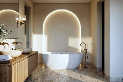 A bathroom with a backlit arched niche behind a freestanding stone tub, brass fixtures and a wall-hung double vanity, Studio Sakaia, Dubai
