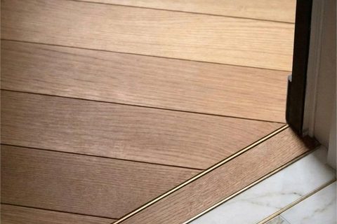 A wide view of the herringbone oak floor meeting marble at a brass threshold line, Studio Sakaia's own Dubai renovation