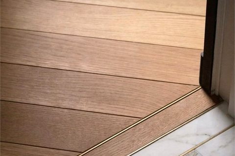 Engineered oak flooring meeting marble at a brass-lined threshold, warm herringbone detail, Studio Sakaia, Dubai