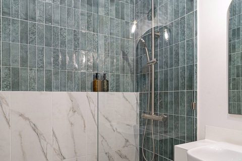 A finished bathroom shower in fluted teal tile and white marble, a rain shower head and brushed nickel column, Studio Sakaia, Dubai