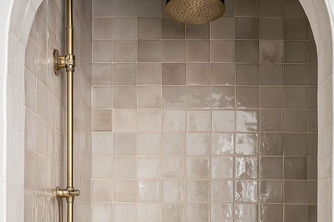 A shower area tiled in Marazzi Gesso zellige-look tile catching the light unevenly, brass rainfall fixture, from Studio Sakaia's own Dubai renovation