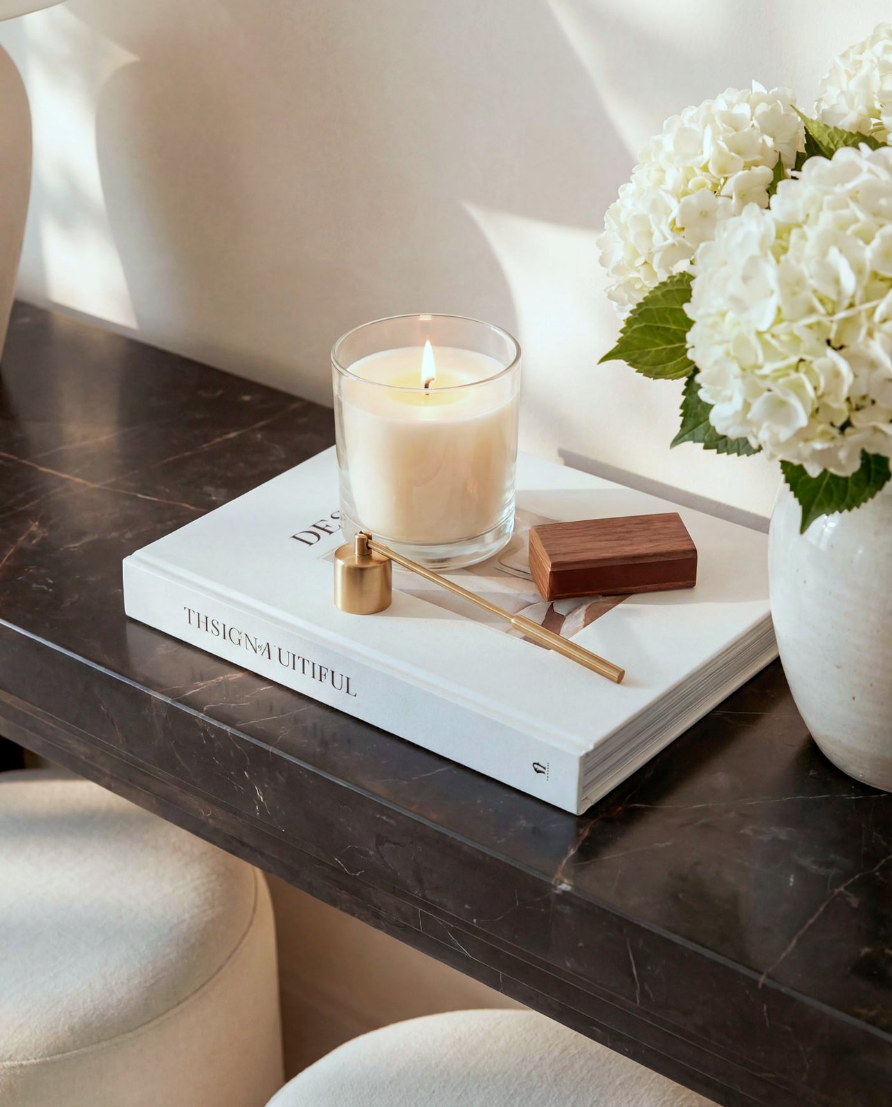 An entry console detail: a lit candle, a design book and white hydrangea on dark stone, Jumeirah townhouse, Dubai