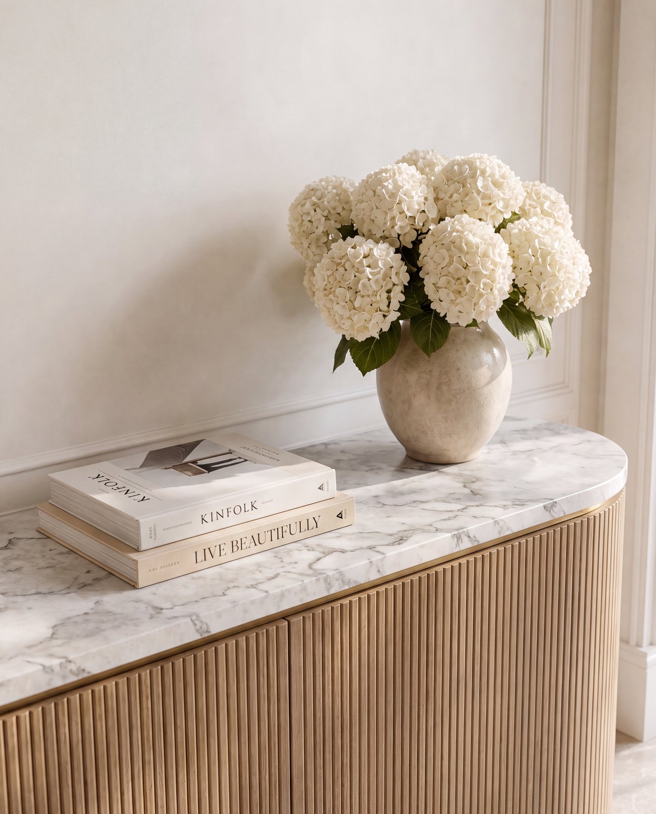 Detail of the Palm Jumeirah entry console: hydrangeas, stacked books and fluted oak in raking daylight, Dubai