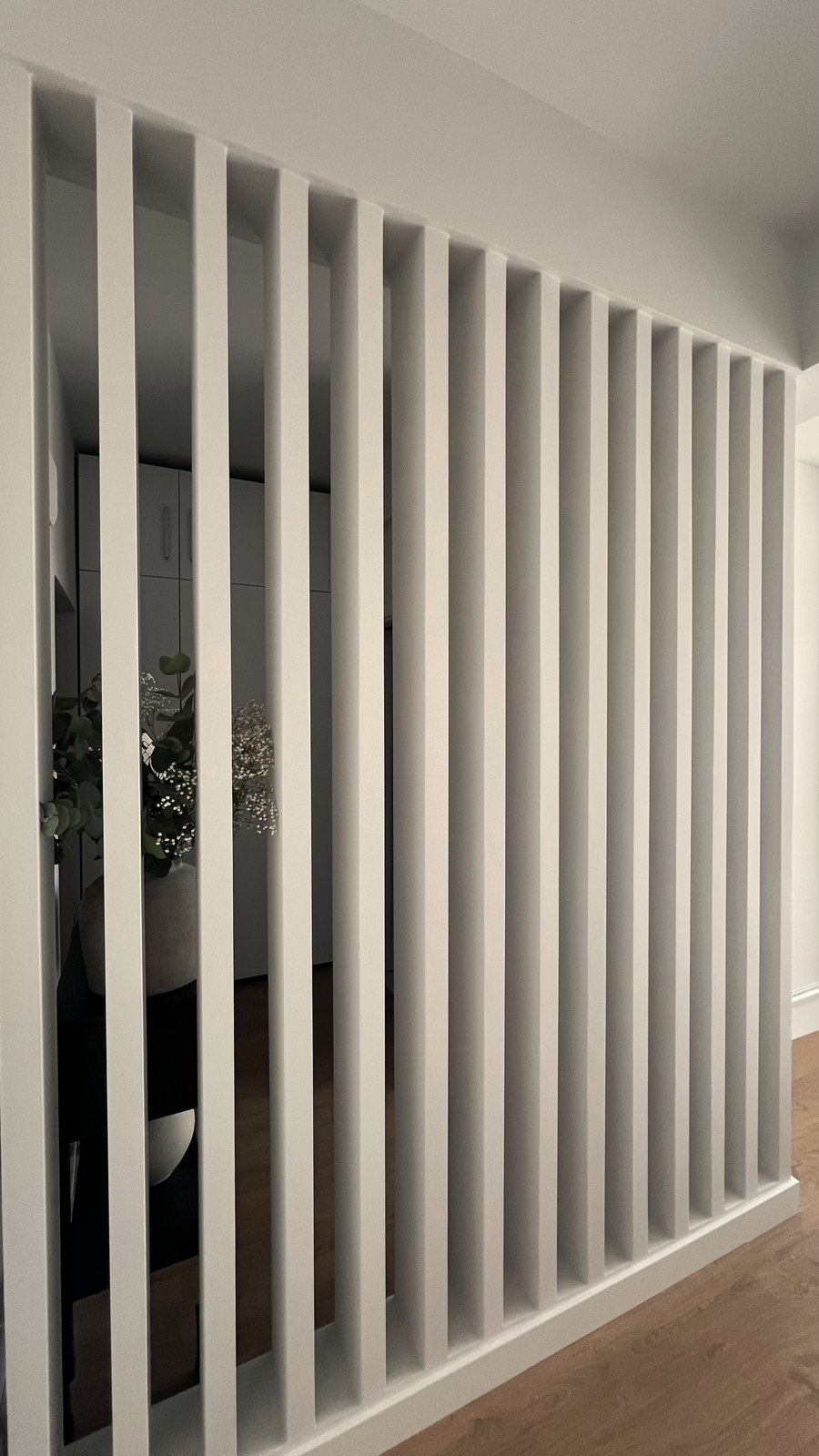 Studio 51 slatted timber screen dividing the entry from the living area, a styled stone vase glimpsed through it, Business Bay, Dubai